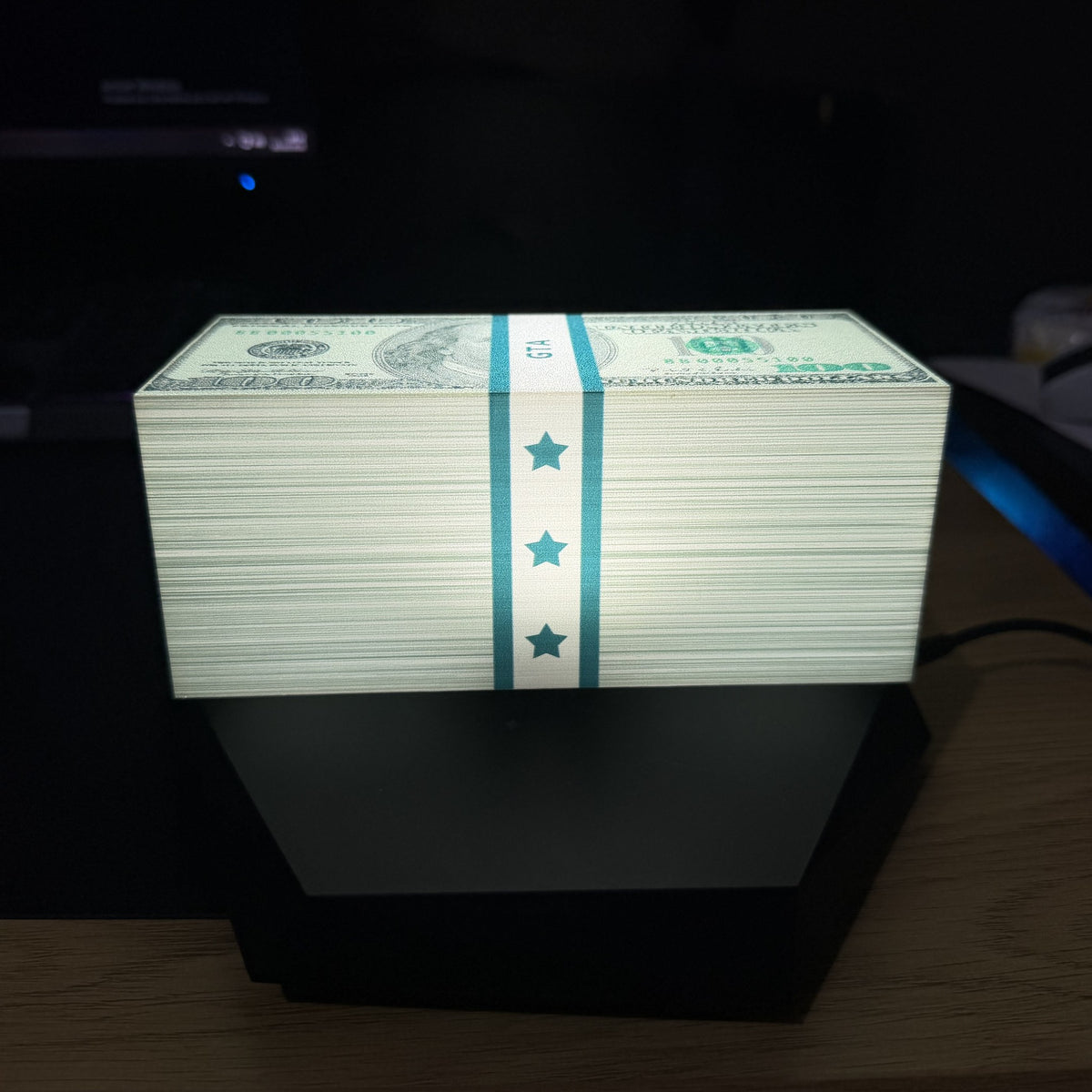 Banknote stack lamp lit in neutral white, three-quarter view on a desk